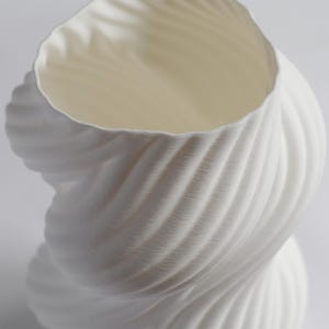 Puede incluir: Un jarr&oacute;n blanco texturizado con un dise&ntilde;o &uacute;nico y retorcido. El jarr&oacute;n tiene una abertura ancha y un interior liso. El exterior presenta una serie de patrones arremolinados y acanalados, creando una apariencia din&aacute;mica y escultural. El jarr&oacute;n est&aacute; hecho de un material blanco mate.