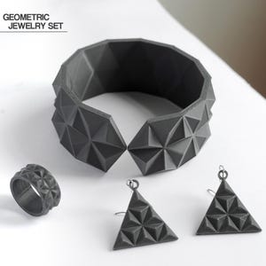 May include: A geometric jewelry set in dark gray, including a bracelet, ring, and two triangular earrings. The bracelet is a wide cuff with a faceted design. The ring and earrings also feature the same geometric pattern. The text "GEOMETRIC JEWELRY SET" is in the upper left.