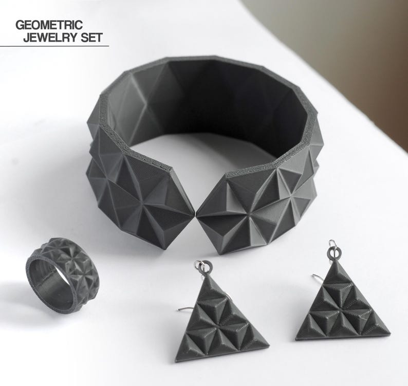 May include: A geometric jewelry set in dark gray, including a bracelet, ring, and two triangular earrings. The bracelet is a wide cuff with a faceted design. The ring and earrings also feature the same geometric pattern. The text "GEOMETRIC JEWELRY SET" is in the upper left.