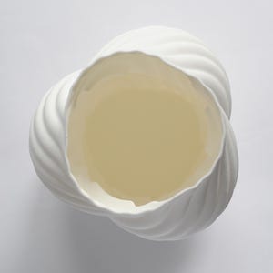 Puede incluir: Un jarr&oacute;n de cer&aacute;mica blanco con un dise&ntilde;o &uacute;nico y ondulado. El interior del jarr&oacute;n es de color amarillo p&aacute;lido. El jarr&oacute;n tiene una superficie texturizada y acanalada y una amplia abertura, ideal para decoraci&oacute;n.