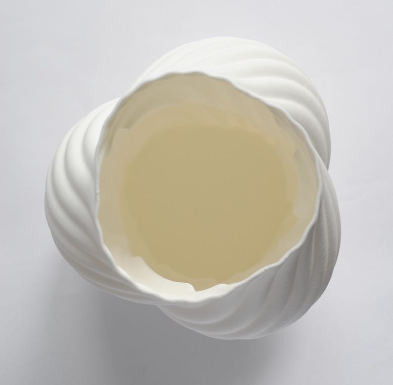 Puede incluir: Un jarr&oacute;n de cer&aacute;mica blanco con un dise&ntilde;o &uacute;nico y ondulado. El interior del jarr&oacute;n es de color amarillo p&aacute;lido. El jarr&oacute;n tiene una superficie texturizada y acanalada y una amplia abertura, ideal para decoraci&oacute;n.