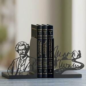 Puede incluir: Un par de sujetalibros de metal negro con una silueta de Mark Twain en un lado y una escena de pesca con el texto Mark Twain en el otro, sosteniendo tres libros titulados Adventures of Huckleberry Finn, Tom Sawyer y A Connecticut Yankee.