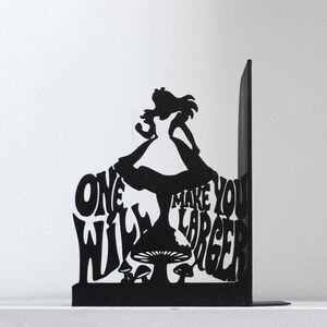 Puede incluir: Un sujetalibros de metal negro con la silueta de una persona de pie sobre una seta. El dise&ntilde;o integra el texto ONE WILL MAKE YOU LARGER en la forma. El objeto tiene una base plana y un panel de soporte vertical en el lado derecho.