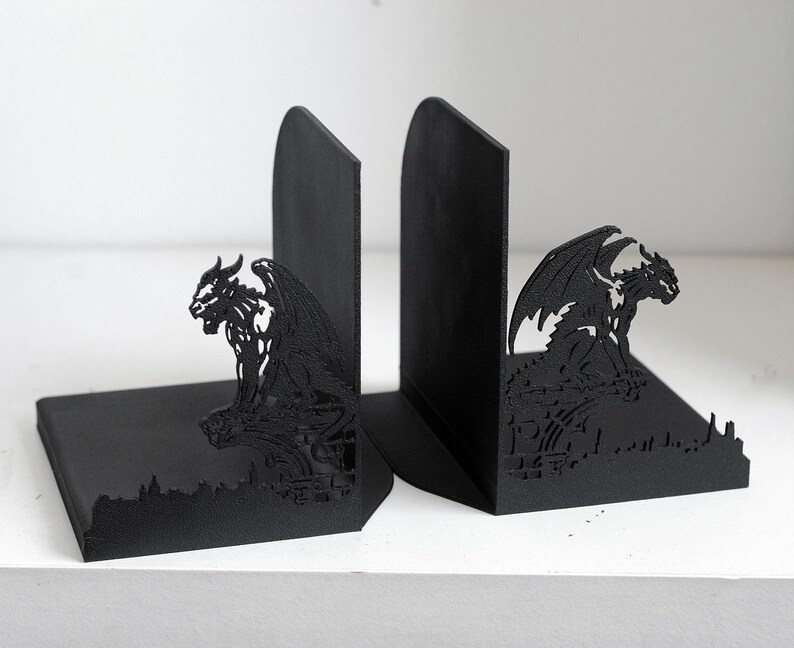 Puede incluir: Par de sujetalibros negros con dise&ntilde;o de g&aacute;rgola g&oacute;tica. Los sujetalibros est&aacute;n hechos de material negro s&oacute;lido y presentan una silueta detallada de una criatura alada posada sobre un paisaje urbano. Est&aacute;n dise&ntilde;ados para mantener los libros en posici&oacute;n vertical.