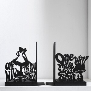 Puede incluir: Un par de sujetalibros de metal negro con dise&ntilde;os de silueta. Uno muestra una figura sobre un hongo con el texto "One will make you larger". El otro muestra una figura junto a un hongo con el texto "One will make you small".