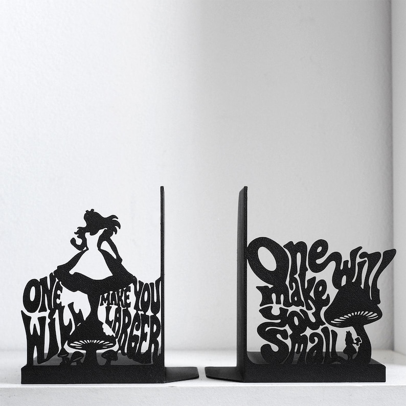 Puede incluir: Un par de sujetalibros de metal negro con dise&ntilde;os de silueta. Uno muestra una figura sobre un hongo con el texto "One will make you larger". El otro muestra una figura junto a un hongo con el texto "One will make you small".