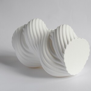 Puede incluir: Una escultura abstracta blanca con un dise&ntilde;o fluido y retorcido. La escultura tiene una superficie texturizada y acanalada y una base circular. La forma general recuerda a una ola o una cinta. La pieza est&aacute; hecha de un material s&oacute;lido y opaco.