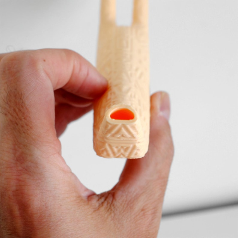 Puede incluir: Un silbato de color melocot&oacute;n claro con un patr&oacute;n geom&eacute;trico en relieve en toda su superficie. La boquilla tiene una abertura interior naranja distintiva y el cuerpo del silbato se extiende hacia arriba con un dise&ntilde;o triangular texturizado.