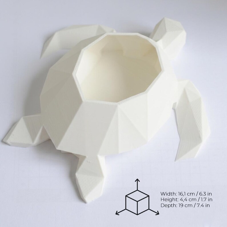 Puede incluir: Una maceta blanca con forma de tortuga geom&eacute;trica. La maceta mide 16,1 cm de ancho, 4,4 cm de alto y 19 cm de profundidad. El dise&ntilde;o presenta una forma poligonal con una abertura central.