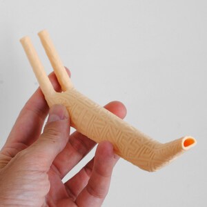 Puede incluir: Un aspirador nasal de pl&aacute;stico en color melocot&oacute;n claro, con forma de Y y un patr&oacute;n geom&eacute;trico texturizado en el cuerpo. El dispositivo tiene dos tubos paralelos en un extremo y una abertura c&oacute;nica en el otro para fines de succi&oacute;n.