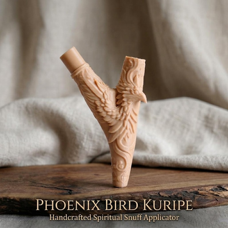 Op de afbeelding: Een beige, Y-vormige applicator met een gebeeldhouwd feniksvogelontwerp. De applicator heeft aan &eacute;&eacute;n uiteinde een cilindrische buis en aan het andere uiteinde een gedetailleerde vogelkop. De tekst "PHOENIX BIRD KURIPIE" en "Handcrafted Spiritual Snuff Applicator" staan onderaan.