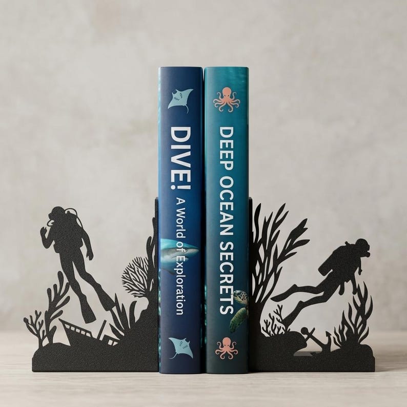 Puede incluir: Dos sujetalibros de metal negro con siluetas de buceadores, arrecifes de coral y naufragios. Sostienen dos libros titulados DIVE! A World of Exploration y DEEP OCEAN SECRETS, que presentan ilustraciones de un tibur&oacute;n, una tortuga marina y pulpos.