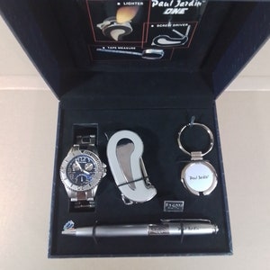 Puede incluir: Un juego de regalo Paul Jardin One plateado en una caja negra. El juego incluye un reloj con una esfera azul, un bolígrafo, un llavero y una multiherramienta.