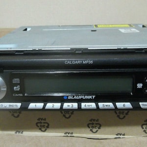 May include: A black car stereo with a silver faceplate and a digital display. The stereo has buttons for source selection, track navigation, and audio settings. The text "CALGARY MP35" and "BLAUPUNKT" are visible on the stereo.