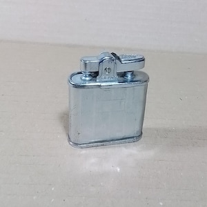 May include: A vintage silver-toned lighter with a rectangular body and a hinged top. The lighter has a textured surface and a small, rectangular area on the front. The word "FIELD" is visible on the top.