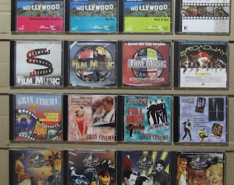 May include: A collection of 18 compact discs (CDs) with various movie soundtracks. The CDs are arranged in three rows of six, with each CD featuring a different movie title and artwork. The titles include "Hollywood", "Film Music", "Gran Cinema", and "Broadway".