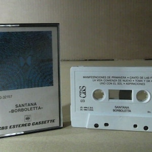 Puede incluir: Una cinta de casete blanca con un diseño de mariposa azul y blanca en la parte delantera. La cinta de casete está etiquetada como "Santana "Borboletta"" y "CBS Estereo Cassette". La parte posterior de la cinta de casete tiene los títulos de las canciones "Manifestaciones de Primavera", "Canto de las Flores", "La vida comienza de nuevo", "Toma y da", "Uno con el sol" y "Aspiraciones".