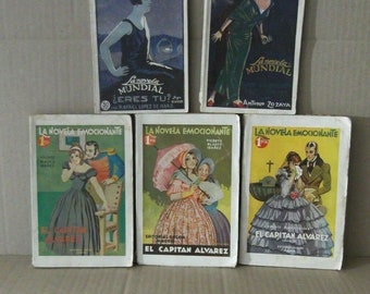 May include: Five vintage paperback books with colourful covers. The covers feature illustrations of people and text that reads "La Novela Emocionante", "La Novela Mundial", "El Capitan Alvarez", and "¿Eres Tu?"