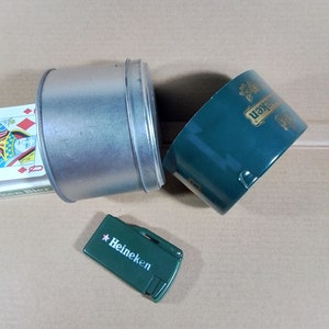 May include: A green metal container with the text "Heineken" on it, a silver metal container, and a green lighter with the text "Heineken" on it.