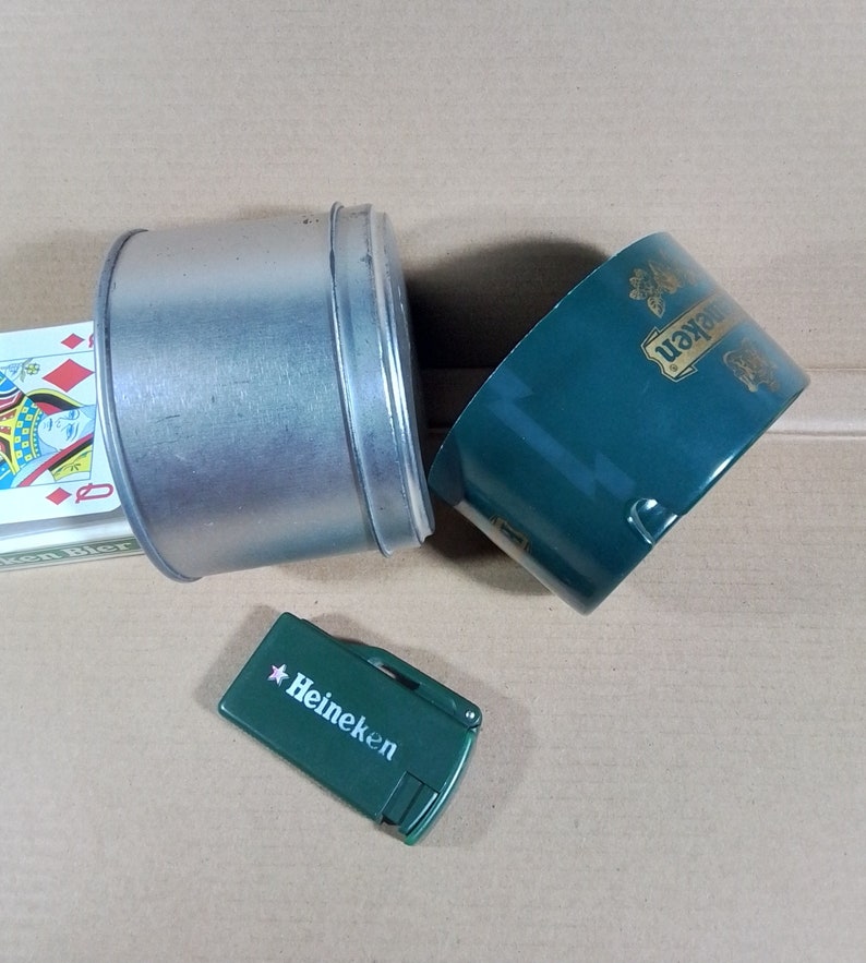 May include: A green metal container with the text "Heineken" on it, a silver metal container, and a green lighter with the text "Heineken" on it.