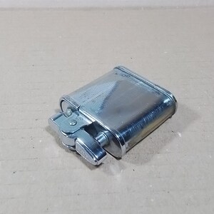 May include: A silver-colored, rectangular lighter with a textured, ridged surface. The lighter has a hinged lid and a side lever for ignition. The design is classic and functional, suitable for everyday use.