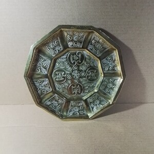 Puede incluir: Bandeja octogonal de latón con un intrincado diseño en relieve. La bandeja tiene una sección central elevada con un patrón floral y un motivo repetitivo alrededor del borde.