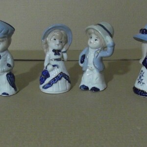 Puede incluir: Conjunto de siete figuras de porcelana de niños que llevan ropa azul y blanca y sombreros. Las figuras están todas de pie y tienen un estilo caprichoso y vintage.