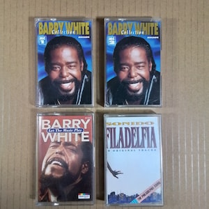 Puede incluir: Cuatro cintas de cassette con la música de Barry White. Las cintas están en estuches de plástico transparente con ilustraciones coloridas. Las dos cintas superiores están etiquetadas como "Barry White Collection" con "MC 1" y "MC 2" en el lado izquierdo del estuche. La cinta inferior izquierda está etiquetada como "Barry White Let The Music Play" y la cinta inferior derecha está etiquetada como "Sonido Filadelfia 8 Original Tracks".
