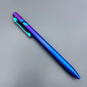 May include: A sleek, metallic pen with a gradient finish, transitioning from purple to blue. The pen features a teal clip and a push-button mechanism. The body of the pen has a textured, ridged design.