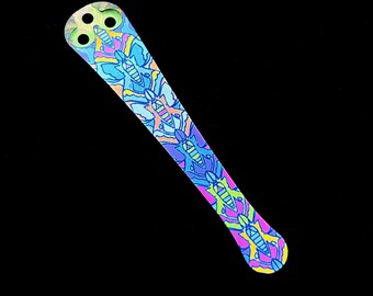 May include: A colourful, patterned, plastic, butterfly-shaped, tool for applying glue or resin. The tool has a pointed tip and a handle with three holes.