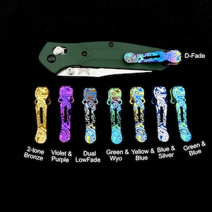 Puede incluir: Un conjunto de diez cachas de navaja de bolsillo de titanio en varias combinaciones de colores, incluyendo bronce de dos tonos, violeta y morado, degradado doble, verde y wyo, amarillo y azul, azul y plata, y verde y azul. Las cachas están todas estampadas con un diseño de remolino. El texto "D-Fade" es visible en la esquina superior derecha de la imagen.