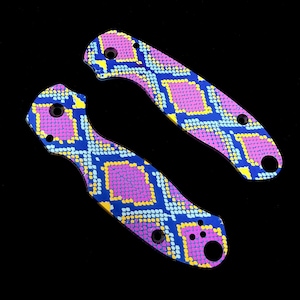 Peut inclure: Deux plaquettes de couteau avec un motif de peau de serpent vibrant. Les plaquettes présentent un motif répétitif de losanges bleus, jaunes et roses. Chaque plaquette comporte plusieurs trous pour la fixation et une forme incurvée.