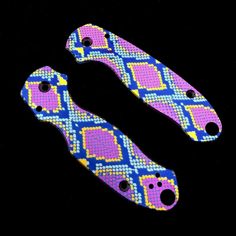 K&ouml;nnte beinhalten: Zwei Messerschalen mit einem lebendigen Schlangenhautmuster. Die Schalen weisen ein sich wiederholendes Design aus blauen, gelben und rosa Diamantformen auf. Jede Schale hat mehrere L&ouml;cher zur Befestigung und eine gebogene Form.