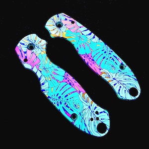 May include: Two knife handle scales featuring a vibrant tropical monstera leaf pattern in shades of bright cyan, magenta, and yellow. Each scale has pre-drilled circular holes for assembly, showcasing a smooth, flat, and contoured shape.