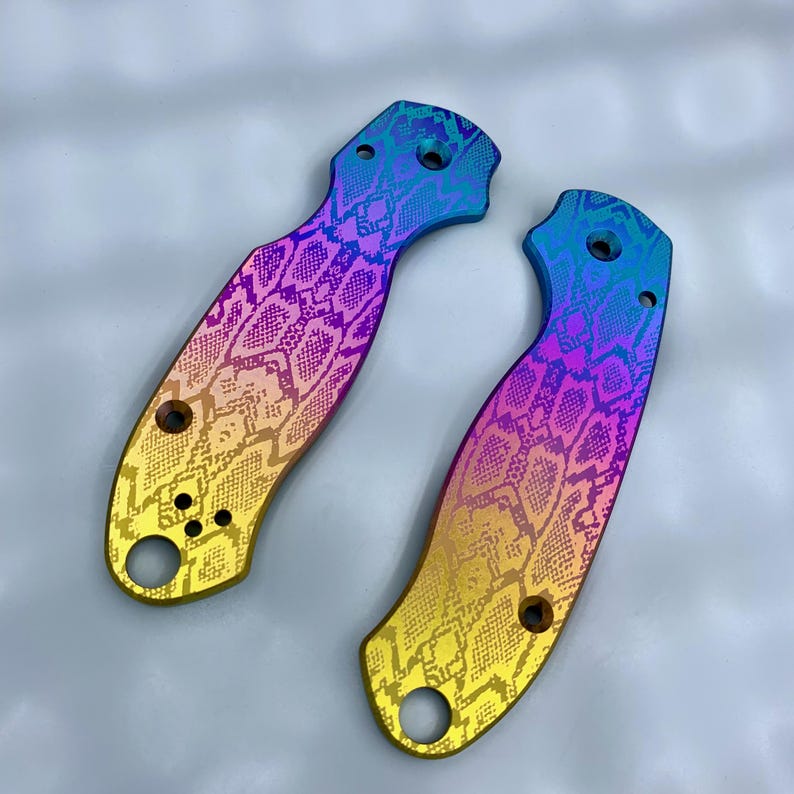 K&ouml;nnte beinhalten: Zwei Messergiffschalen mit einem lebendigen Regenbogen-Finish und einem Schlangenhautmuster. Die Schalen haben eine gebogene Form mit mehreren L&ouml;chern f&uuml;r Schrauben. Die Farben gehen von Gelb &uuml;ber Lila bis Blau.