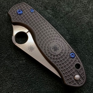 May include: A black Spyderco Para 3 folding knife with blue screws and a textured black handle. The knife has a partially open blade and a Spyderco logo on the blade.