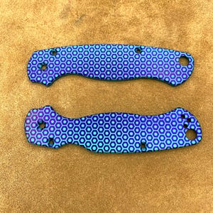 May include: Two knife handle scales with a blue and purple honeycomb pattern. Each scale has multiple holes for screws and a lanyard hole. The scales are made of a durable material and are designed to replace existing knife handles.
