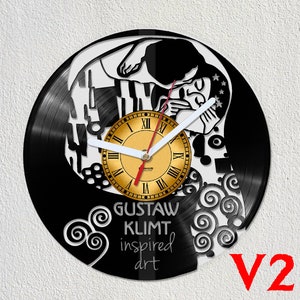 Puede incluir: Un reloj de vinilo negro con un diseño blanco que representa a una pareja abrazándose. La esfera del reloj es dorada con números romanos y agujas negras. El texto "Gustav Klimt inspired art" está impreso debajo de la esfera del reloj.
