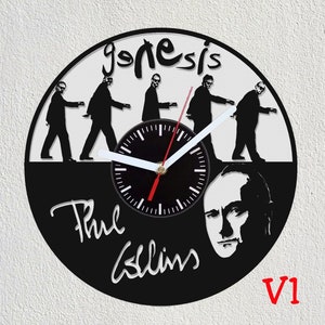 Peut inclure: Horloge en vinyle noir et blanc représentant une silhouette du groupe Genesis, avec le texte "Genesis" en haut et "Phil Collins" en bas. Le cadran de l'horloge est noir avec des aiguilles blanches et une bordure blanche. L'horloge est étiquetée "V1" dans le coin inférieur droit.