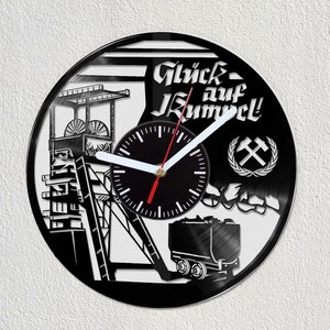 May include: Black vinyl record clock with a white clock face and hands. The clock features a black and white silhouette of a mine shaft with a coal cart and the text "Glück auf Kumpel!" and a pickaxe and wreath.