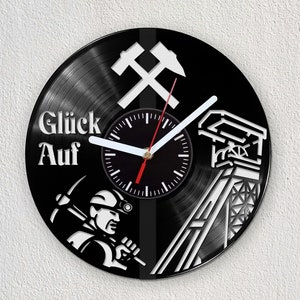 May include: Black vinyl record clock with a white design of a miner, a mine shaft, and crossed pickaxes. The clock face is black with white numbers and hands. The text "Glück Auf" is printed in white on the clock.