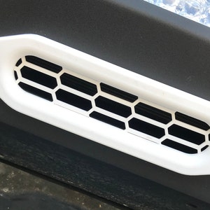 May include: White plastic vent with a black honeycomb grille. The vent is oval shaped and has two screws on either side.