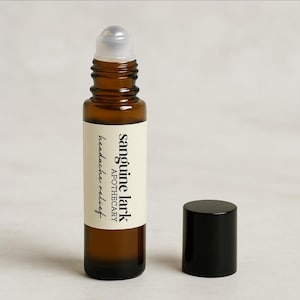May include: A brown glass roller bottle with a white label that reads "sanguine lark apothecary headache relief". The bottle has a black cap.