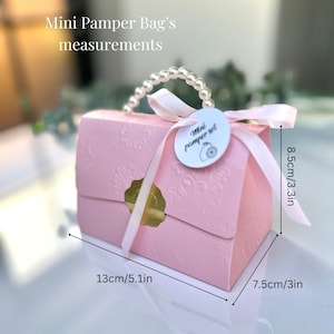 May include: A pink gift box with embossed floral patterns, a pearl handle, and a ribbon. The box is labeled "Mini Pamper Set" and measures 5.1 inches long, 3 inches wide, and 3.3 inches high.