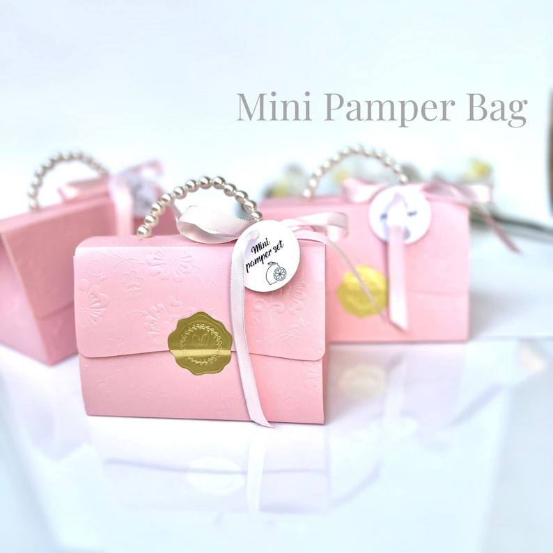 May include: Pink gift bags with embossed floral patterns, pearl handles, and satin ribbons. Each bag features a gold seal and a tag that reads "Mini pamper set". The bags are arranged on a white surface.