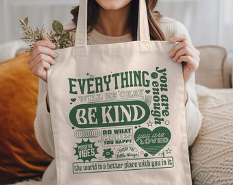 May include: Cream-colored tote bag with green text that reads "Everything will be okay, Be Kind, Positive Vibes, You are enough, You are loved." The bag also has the text "Do what makes you happy" and "Enjoy the little things."