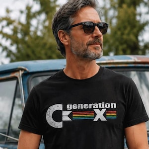 May include: Black t-shirt with the text "generation X" in white and a retro-style graphic. The graphic includes a stylized "C" and "X" with a rainbow-colored stripe. The shirt is worn by a person wearing sunglasses and jeans.