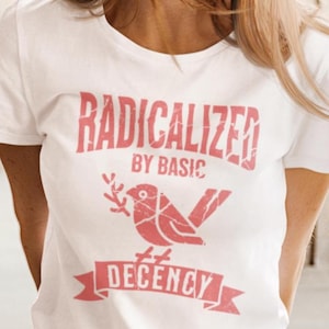 Op de afbeelding: Wit T-shirt met een verweerde rode print. De print bevat de woorden "RADICALIZED BY BASIC DECENCY" en een vogel met een takje. Het shirt met korte mouwen is gemaakt van zacht materiaal.