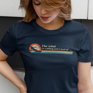 May include: A navy blue t-shirt with a retro-style graphic of a person waterskiing with the text "The wind is calling and I must go".