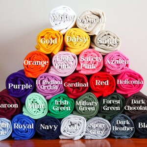 May include: A pyramid of rolled fabric swatches in various colors, including white, gold, orange, purple, maroon, light blue, royal blue, navy, ash, sport grey, dark heather, black, light pink, safety pink, azalea, radiant orchid, cardinal, red, heliconia, mint, irish green, military green, forest green, and dark chocolate.